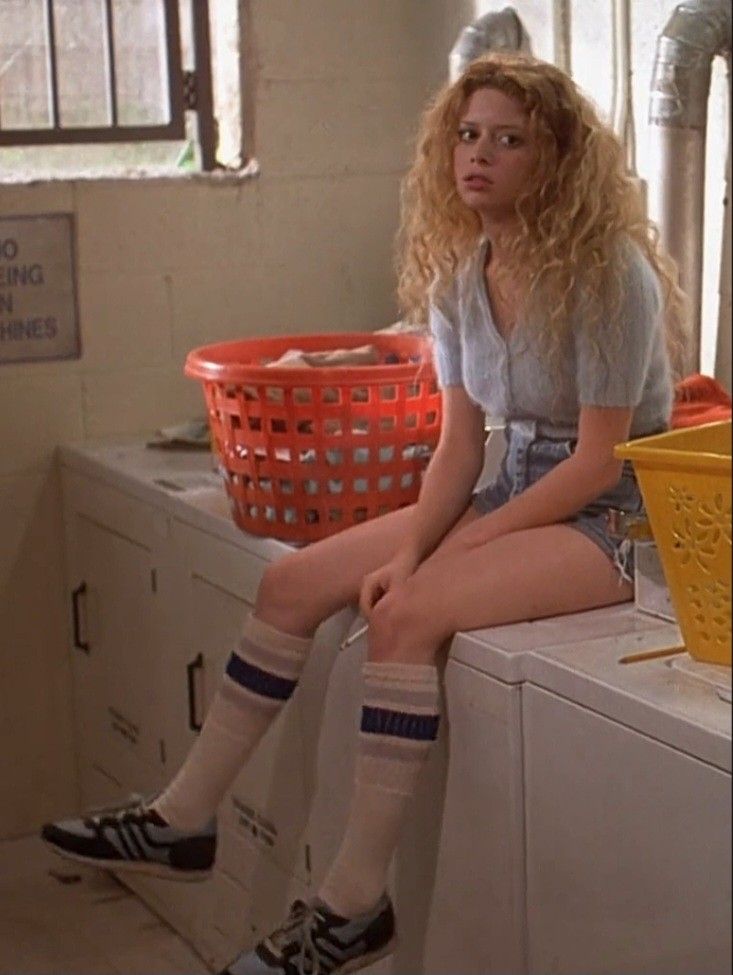 a woman sitting on top of a washer next to a yellow basket and sink