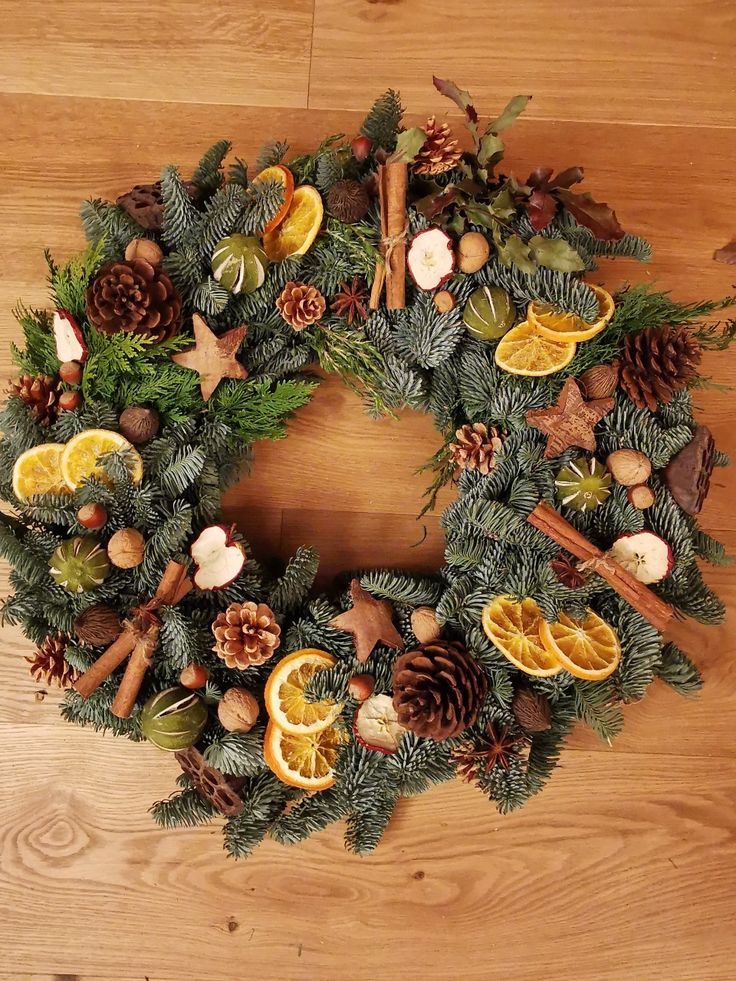 a christmas wreath with oranges, pine cones and cinnamon sticks on a wooden floor