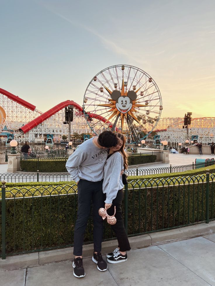 a man and woman standing next to each other near a ferris wheel at an amusement park