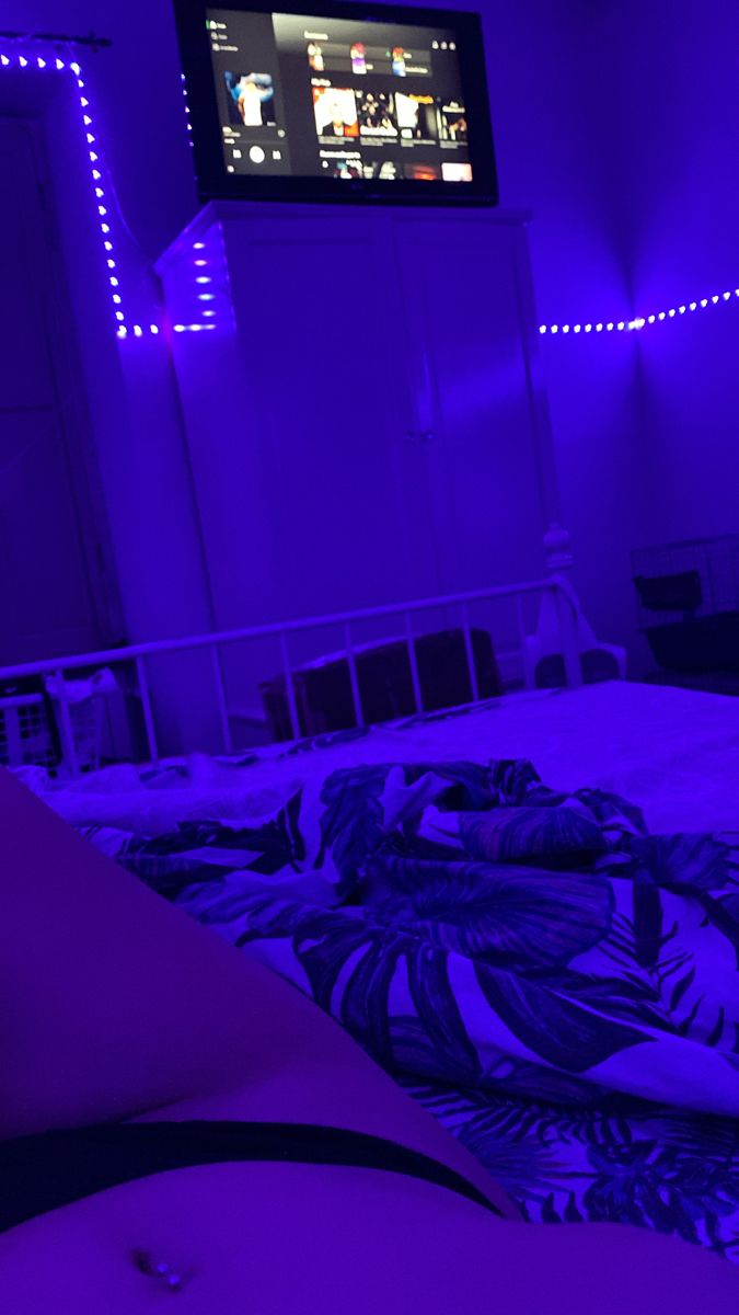 a bed in a room with purple lights and a tv on top of the headboard