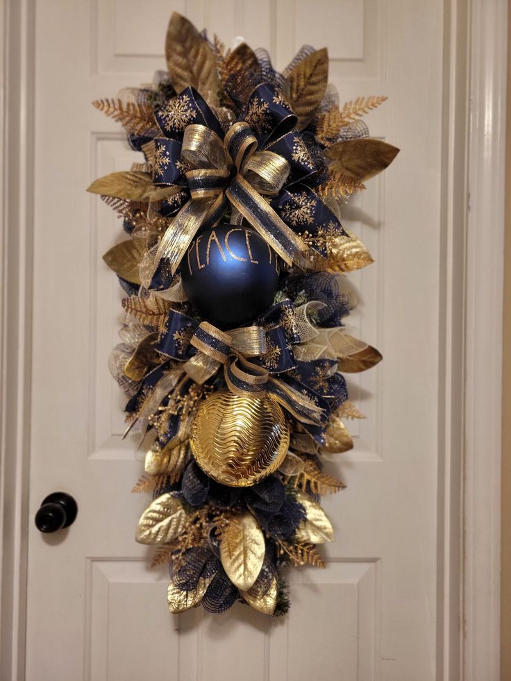 a blue and gold wreath hanging on the front door with an ornament in it