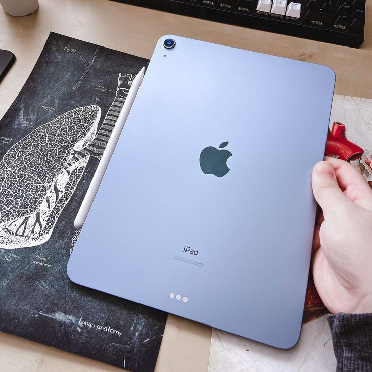 a person holding an apple ipad in front of a keyboard and mouse on a desk