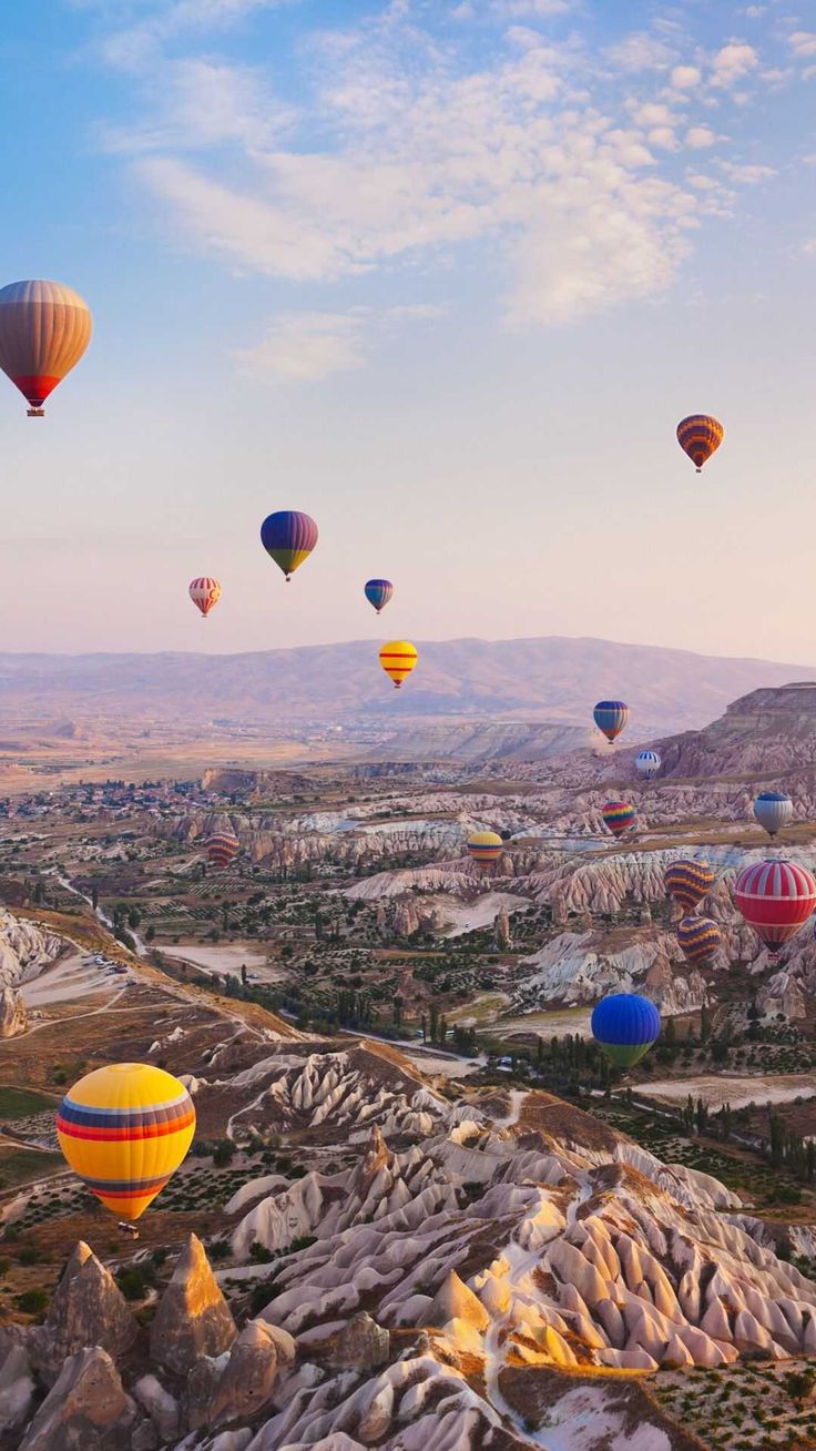 many hot air balloons are flying in the sky above some rocks and trees, with mountains in the background