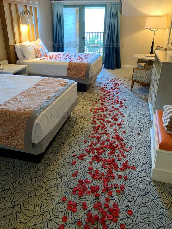 two beds in a hotel room with rose petals on the floor next to each other