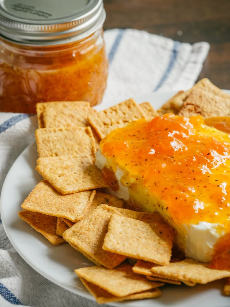 a white plate topped with cheese and crackers next to a jar of honey syrup