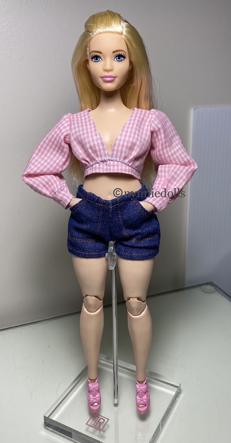 a barbie doll is standing on a glass stand with her hands on her hips and wearing high heels