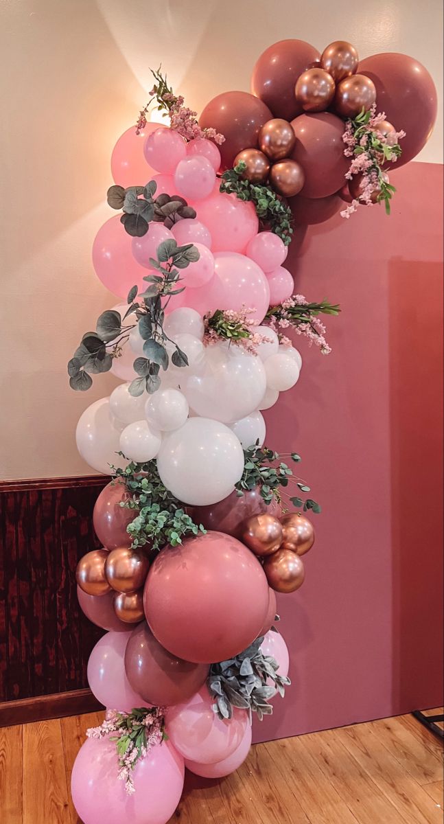 balloons and greenery are arranged on the wall to create a balloon arch for an event