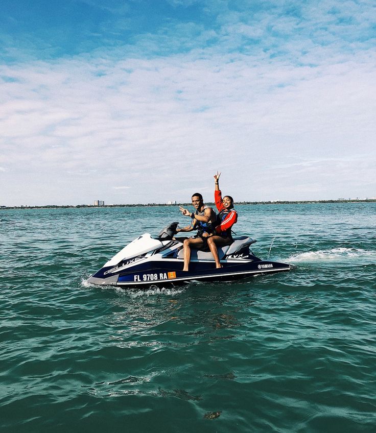 two people riding on the back of a jet ski in the middle of the ocean