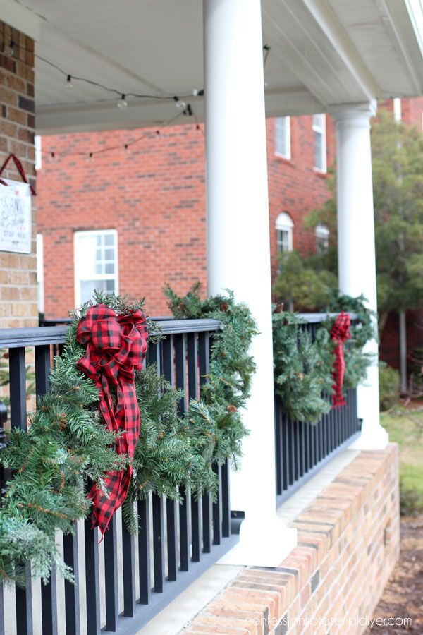 christmas wreaths are hung on the railing of a house with red and black plaid ribbon