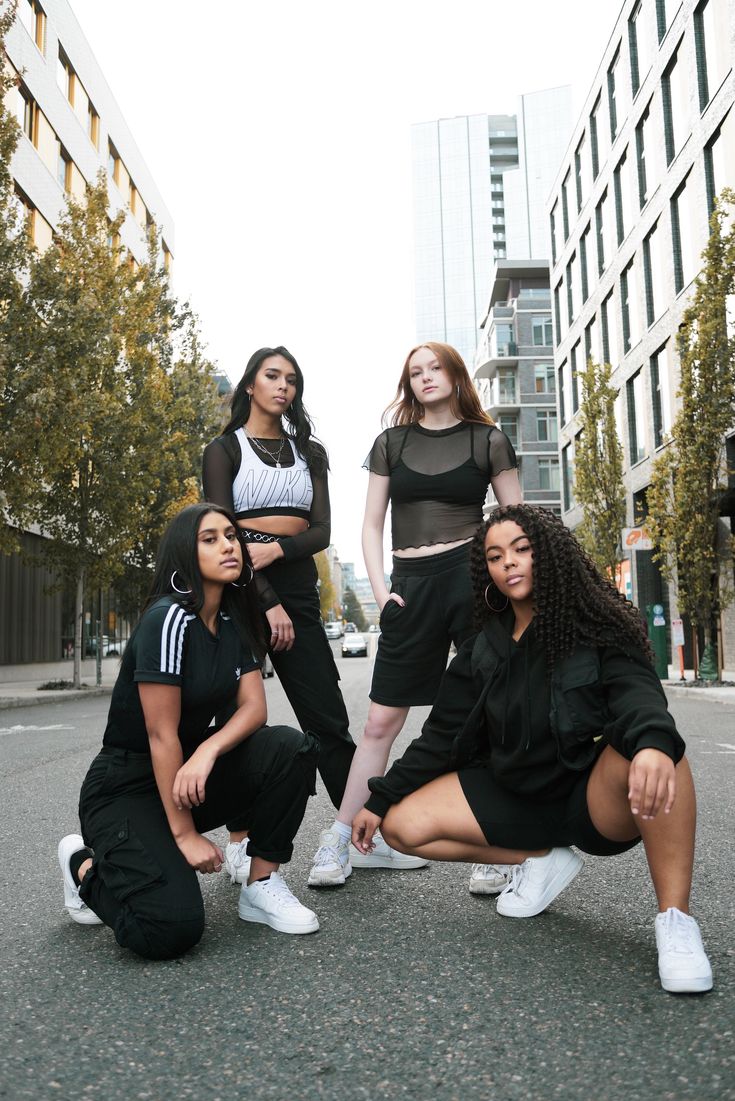 four young women posing in the middle of an empty street with tall buildings behind them