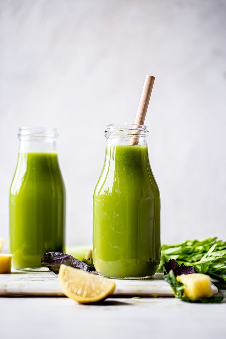 two mason jars filled with green smoothie next to lemon slices and celery