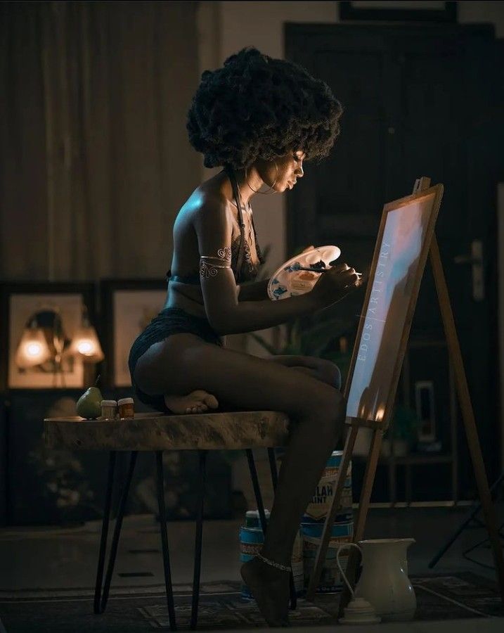 a woman sitting on top of a table next to an easel