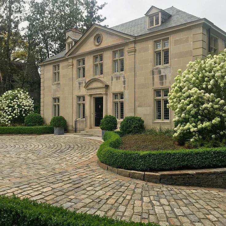 a large house with many windows and bushes in front of it on a cobblestone driveway