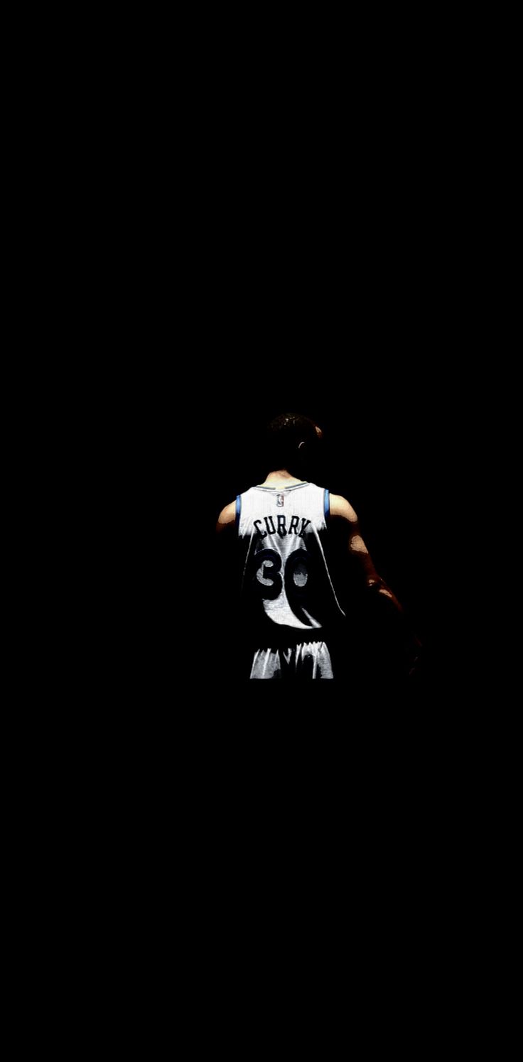 a basketball player is standing in the dark with his back turned to the camera,