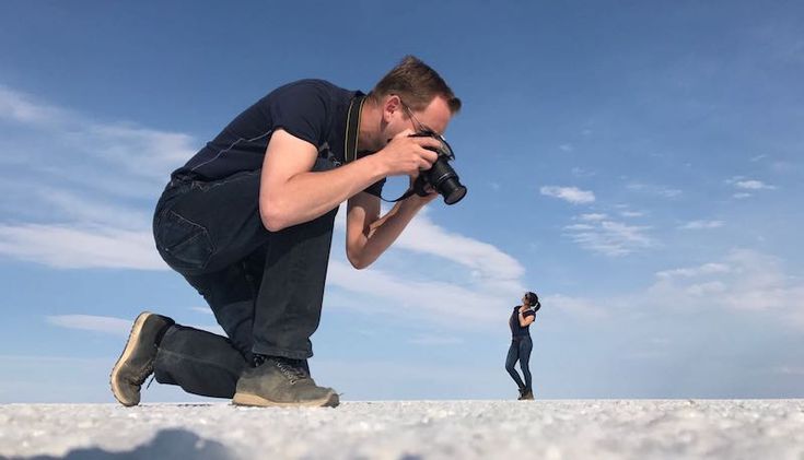 a man kneeling down with a camera in his hand and another person standing behind him