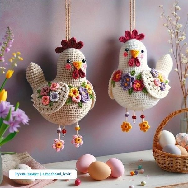 two crocheted chicken ornaments hanging from strings next to eggs and flowers on a table