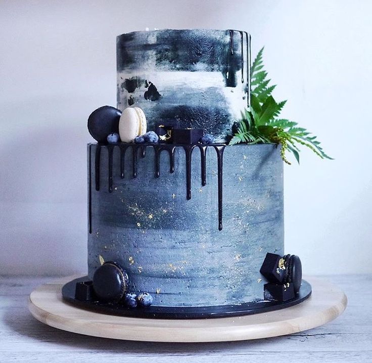 a blue cake with black icing and some plants on the top is sitting on a plate