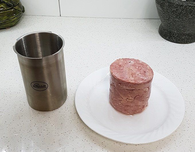 a plate with a piece of meat on it next to a stainless steel coffee cup