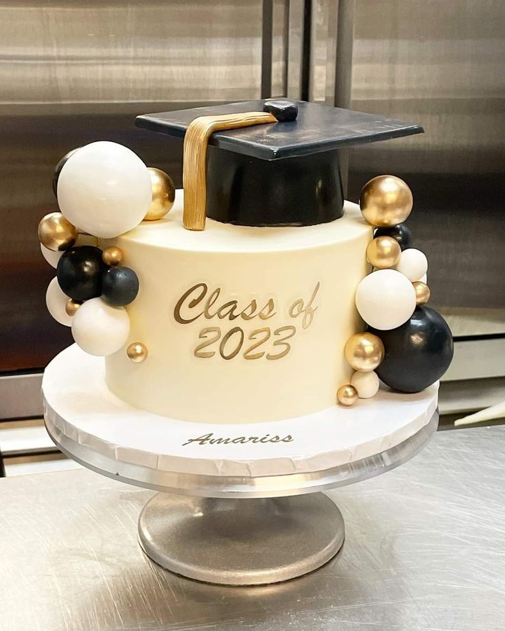 a graduation cake decorated with black, white and gold balloons