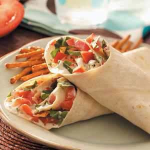 two wraps are sitting on a plate with french fries and tomato wedges next to them