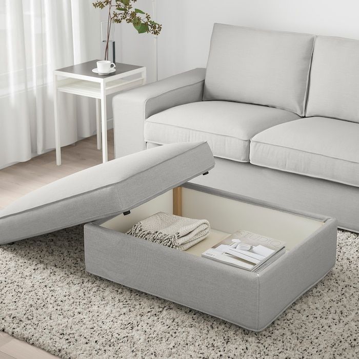 a living room scene with focus on the couch and ottoman that has been opened to reveal an open storage compartment