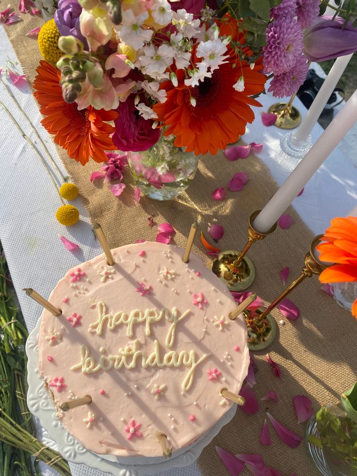 a birthday cake sitting on top of a table with flowers in the vases behind it