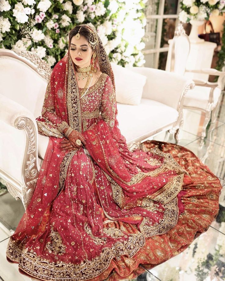 a woman sitting on top of a white couch wearing a red and gold wedding dress