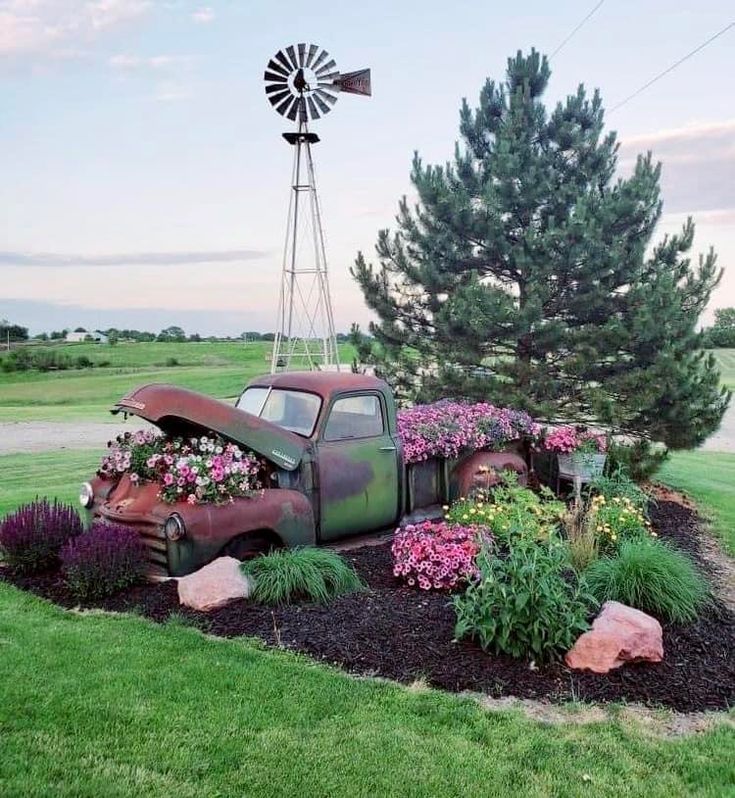 an old truck with flowers and windmill in the back