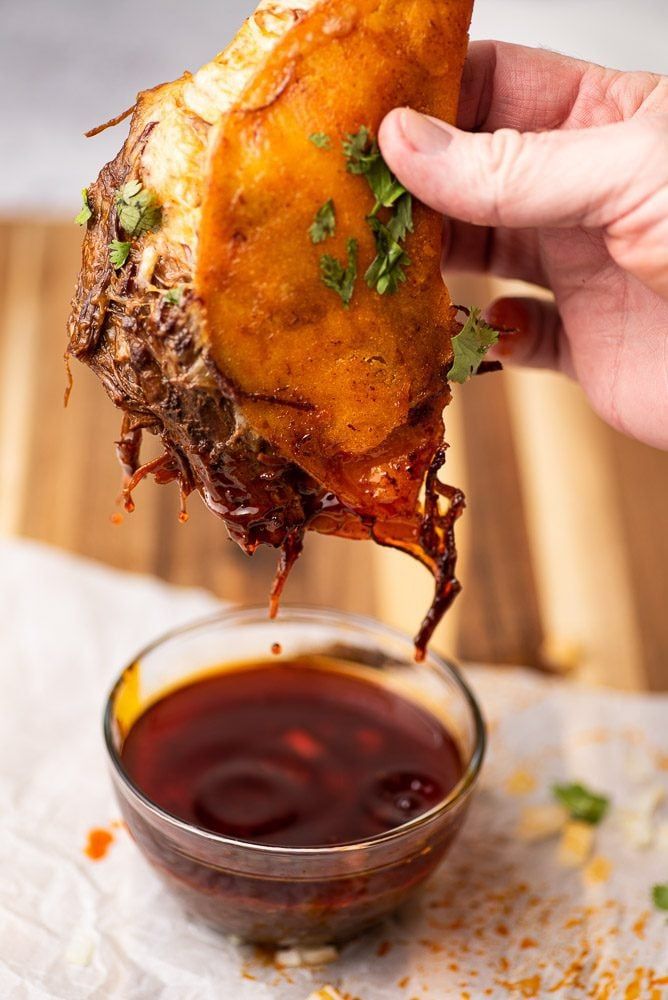 a person dipping sauce on top of a piece of food in a small glass bowl