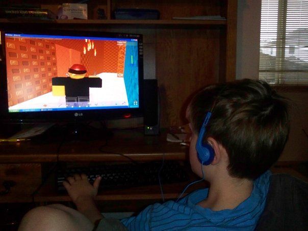 a young boy sitting in front of a computer monitor with headphones on his ears