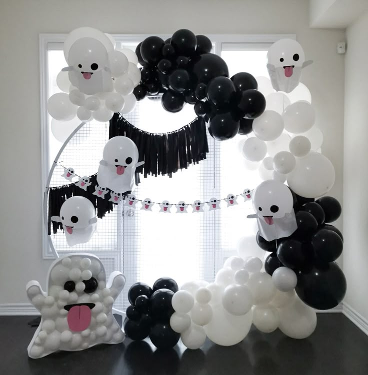 black and white balloons are hanging in front of a window with ghost faces on it