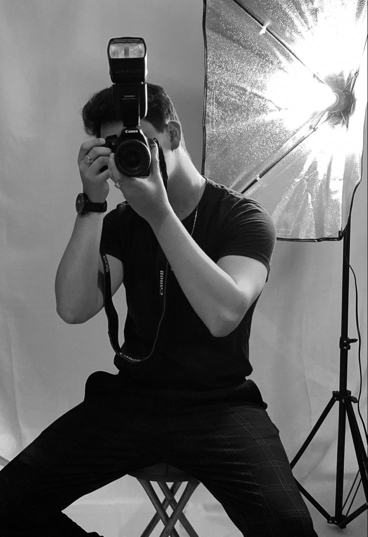 a man sitting in front of a camera taking a photo with an umbrella behind him