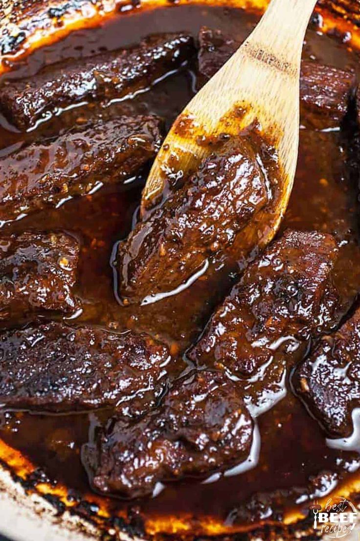 a wooden spoon in a pot filled with beef and gravy on the stove