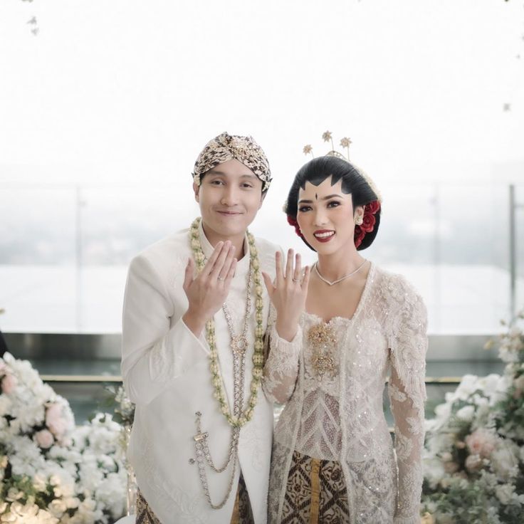 a man and woman standing next to each other in front of white flowers with their hands together