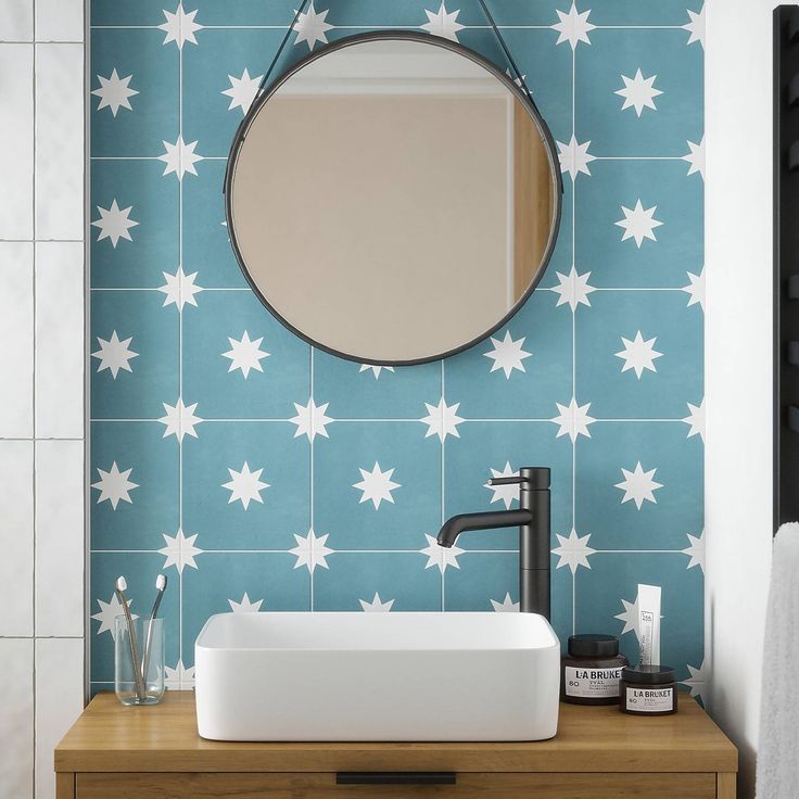 a bathroom sink with a round mirror on the wall above it and a blue star patterned wall paper behind it