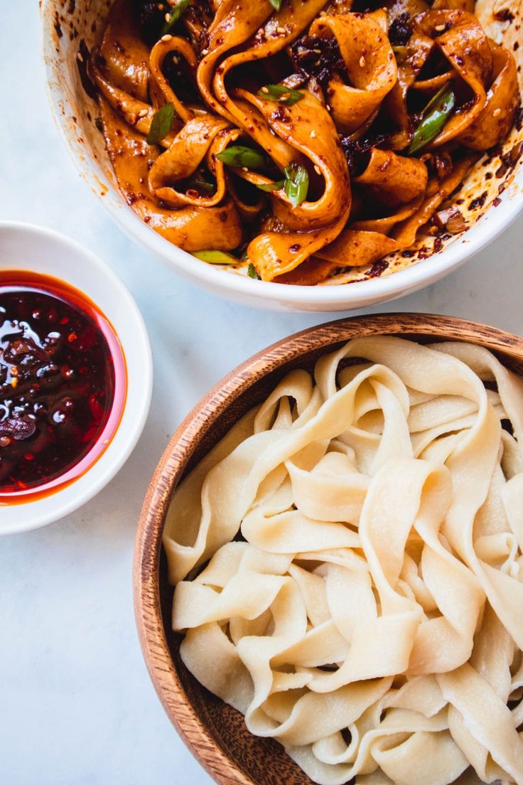 two bowls filled with pasta and sauce next to another bowl full of noodles on a table