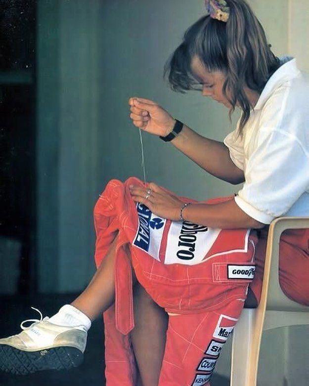 a woman sitting on top of a white chair next to a red bag and wearing pink pants