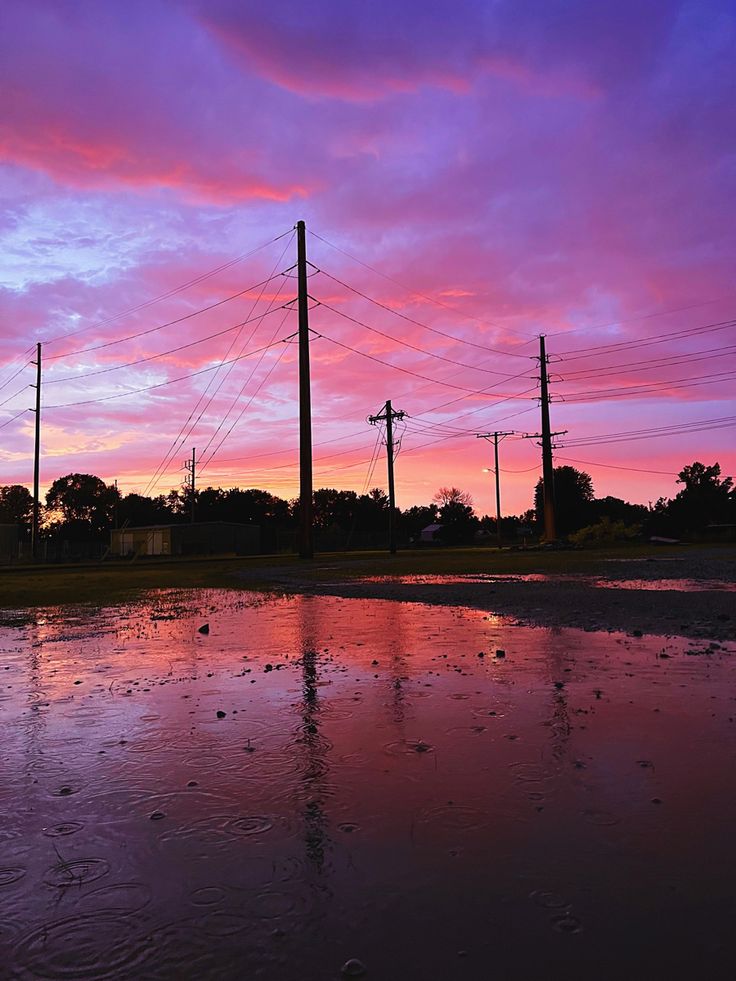 the sky is pink and purple as it sits on top of puddles in front of power lines