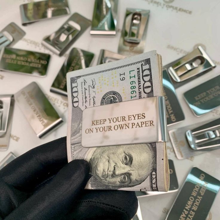 a person holding money in their hand with other metal objects scattered around them on top of a table