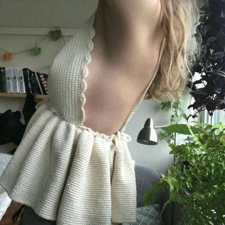 the back of a woman's sweater in front of a plant and bookshelf