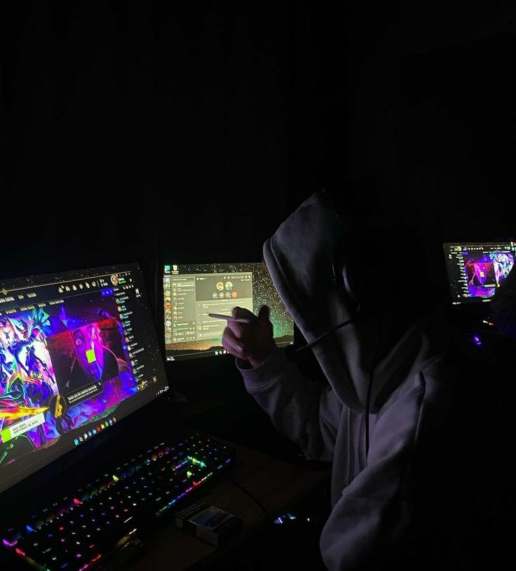 a person sitting in front of two computer monitors with colorful lights on them at night