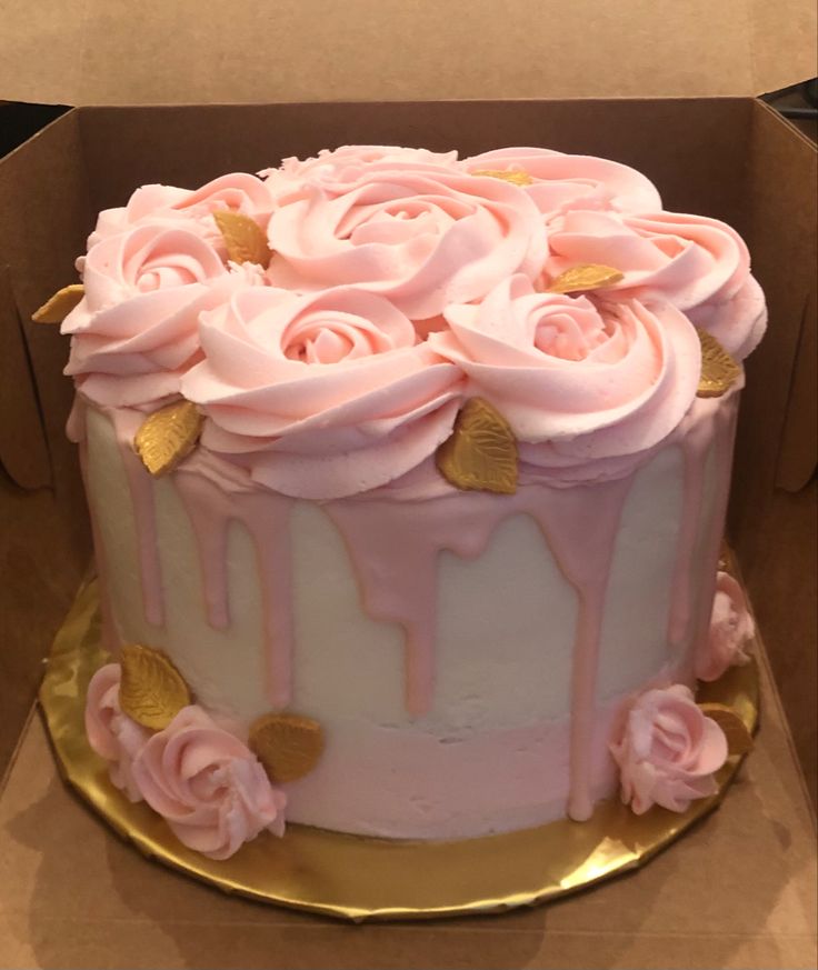 a pink cake with white frosting and roses on top in a cardboard box, ready to be eaten