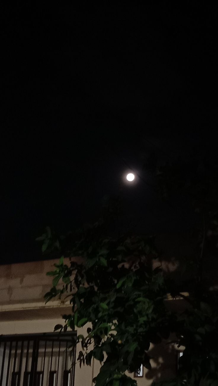 the moon is shining brightly in the dark night sky over a building with shutters