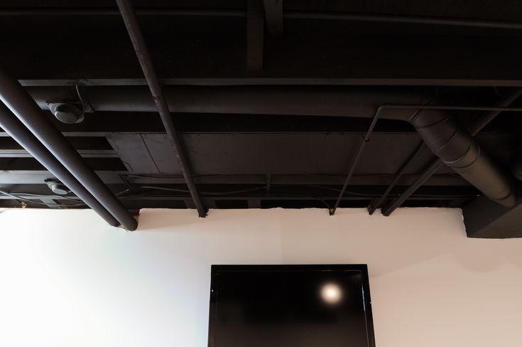 an overhead view of a room with white walls and black pipes on the ceiling, in front of a flat screen tv