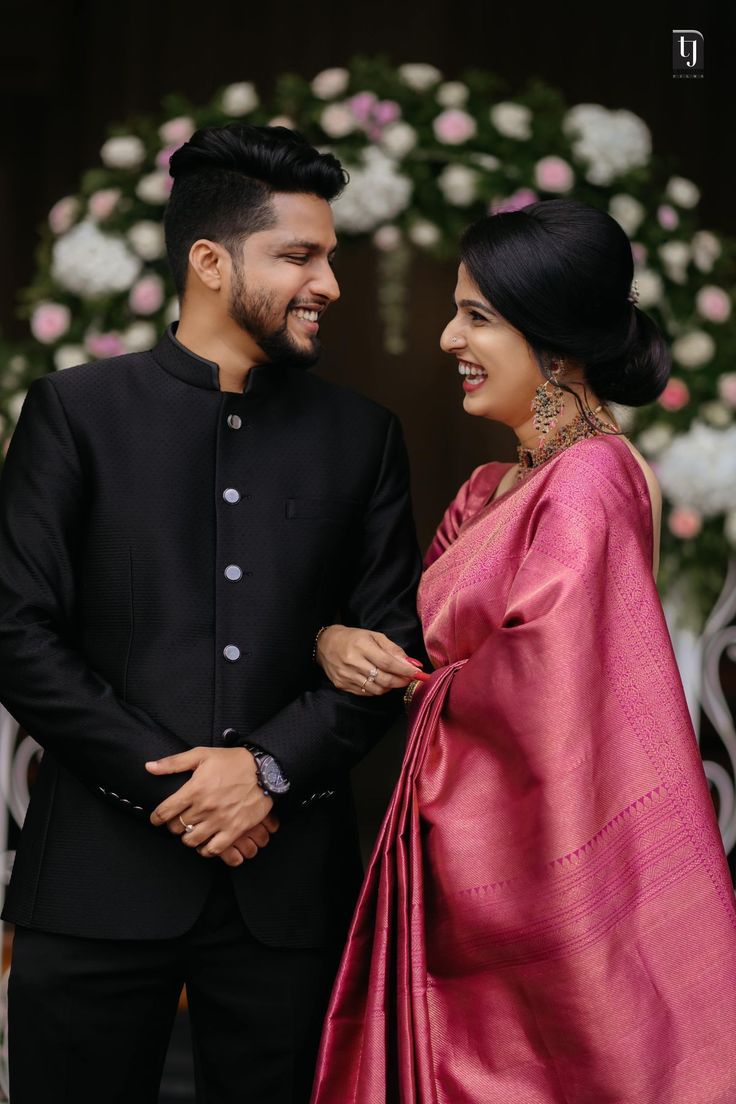 a man and woman standing next to each other in front of a floral arch holding hands