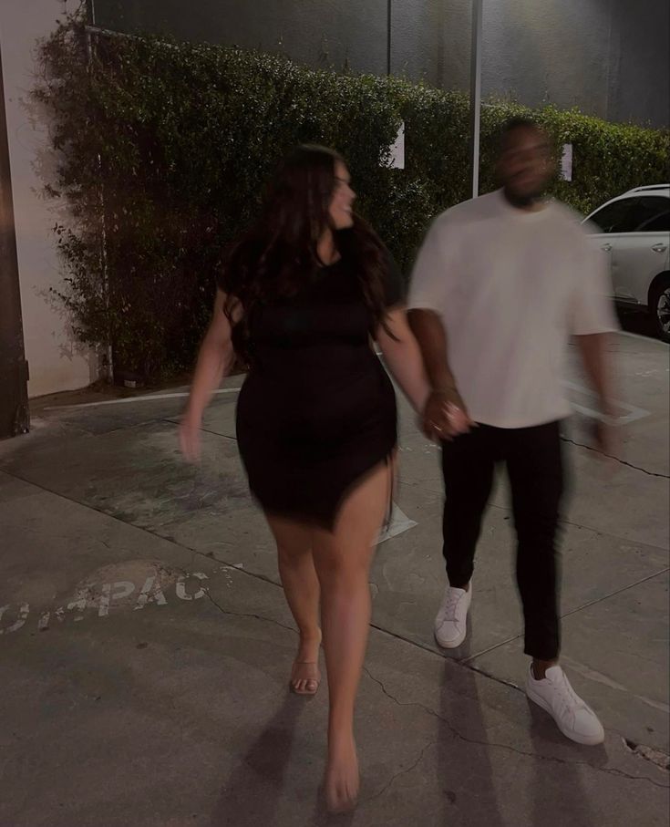 a man and woman are walking down the street at night, one is holding hands