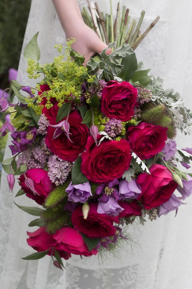 a bride holding a bouquet of red and purple flowers with greenery in her hand