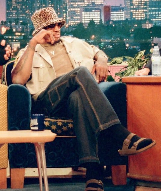 a man sitting in a chair talking on a cell phone while wearing a leopard print hat