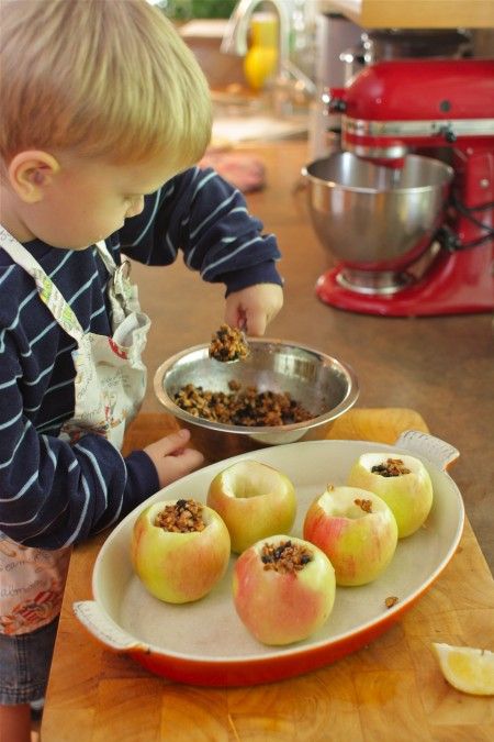 a little boy that is standing in front of some apples on a plate with granola