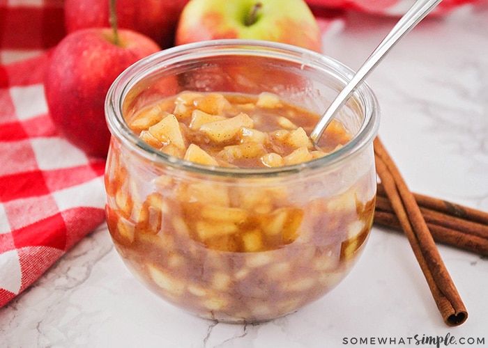 apples and cinnamon in a glass jar with spoons on the table next to them